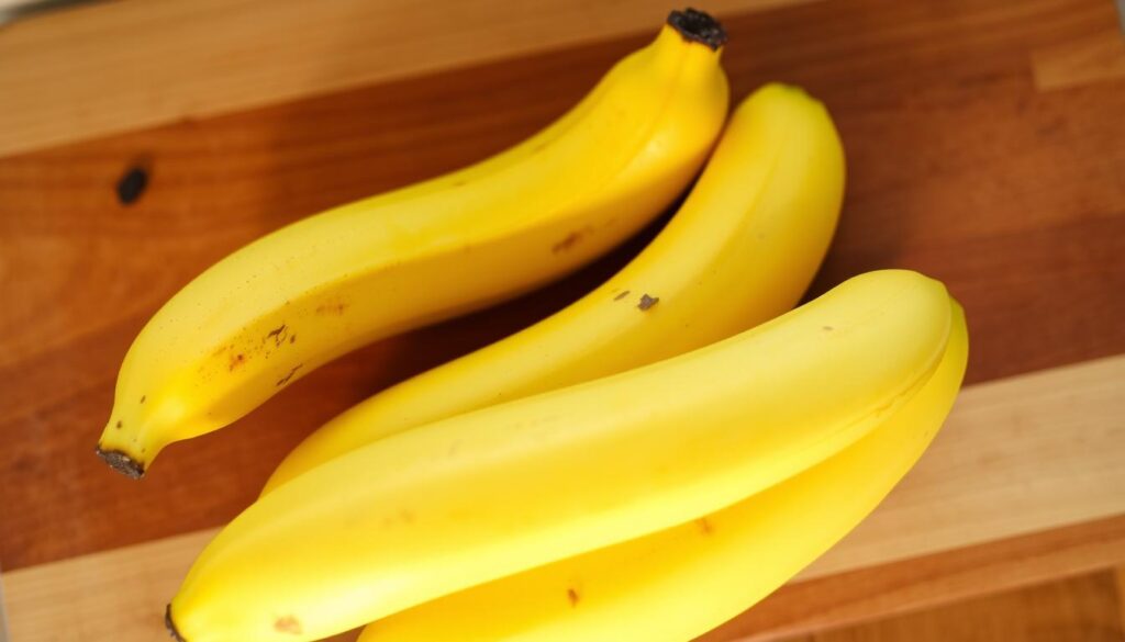 Ripe, golden-yellow bananas nestled on a wooden cutting board, their peels slightly speckled with brown flecks, signaling their perfect ripeness for moist, fluffy banana bread. Soft, ambient lighting from above casts a warm, inviting glow, highlighting the natural curves and texture of the fruit. The bananas are arranged in an artful, visually appealing composition, ready to be mashed and incorporated into a delectable baked good. The overall scene exudes a cozy, homemade atmosphere, capturing the essence of essential ingredients for the perfect loaf of banana bread.